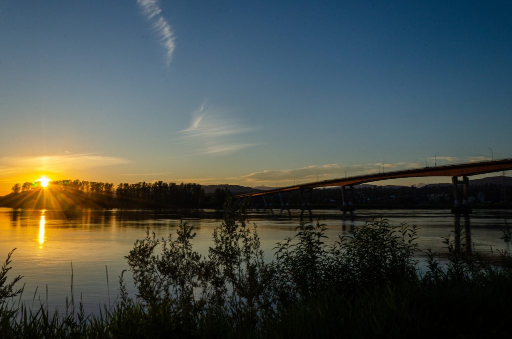 A scenic sunset view of a river with a silhouette of a bridge and trees, creating a tranquil atmosphere. Visit a dentist near you to maintain a bright smile.