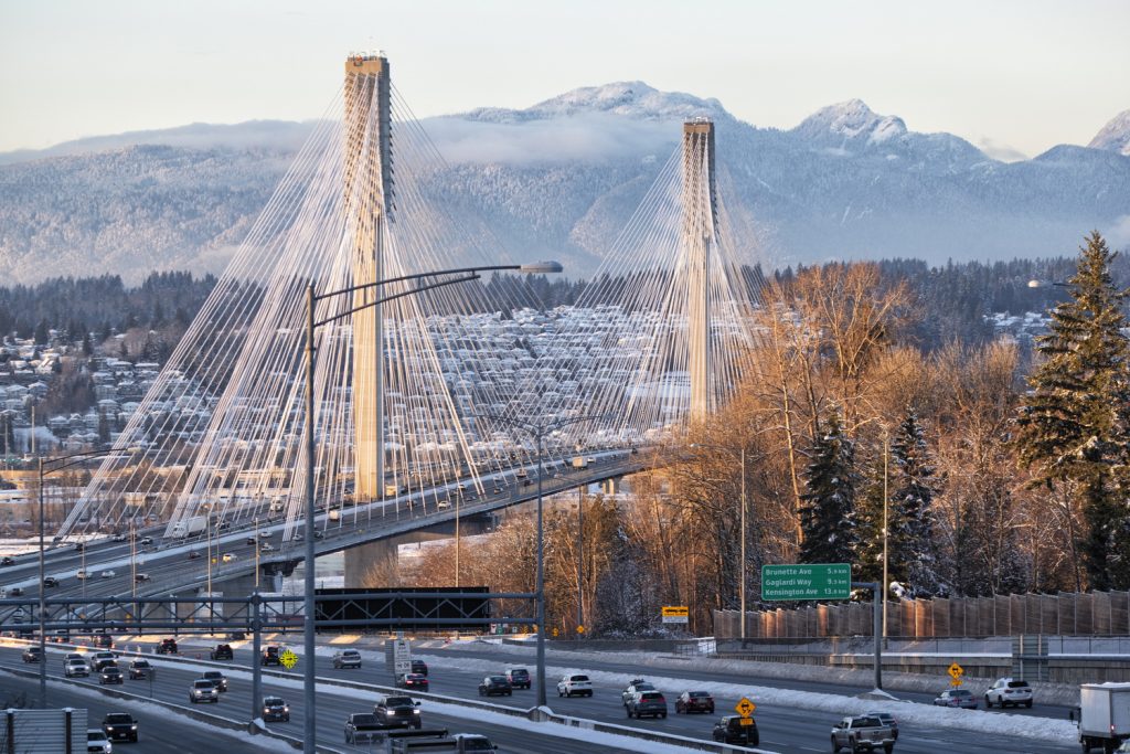 A view of a suspension bridge with mountains in the background, surrounded by trees. A blue smiling face is superimposed in the sky above the bridge.