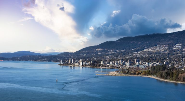 Coastal city skyline at dusk with mountains in the background and a large smiling blue face icon in the sky.