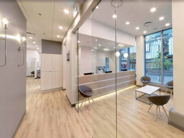 A modern, well-lit reception area featuring a sleek desk, comfortable seating, and large windows. The design includes wooden flooring and minimalistic decor, creating a welcoming atmosphere.