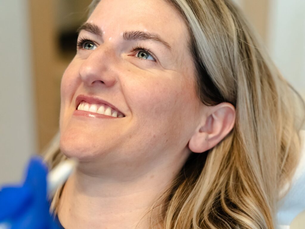 A woman with blonde hair smiles while sitting in a dental chair, looking relaxed and content. The setting appears to be a dental clinic, emphasizing a positive dental experience.