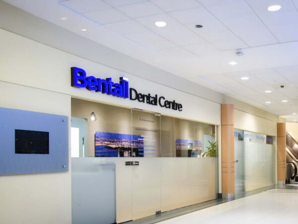 A modern dental clinic reception area featuring the sign "Bental Dental Centre." The space is well-lit, with glass walls and an inviting atmosphere.