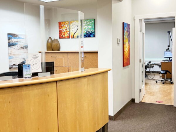 A bright and welcoming reception area features a curved wooden desk, colorful artwork on the walls, and a doorway leading to another room. The space is clean and modern, providing a friendly atmosphere for visitors.