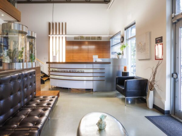 A modern reception area featuring a sleek front desk, comfortable leather seating, and large windows allowing natural light. Decorative plants and an aquarium enhance the welcoming atmosphere.