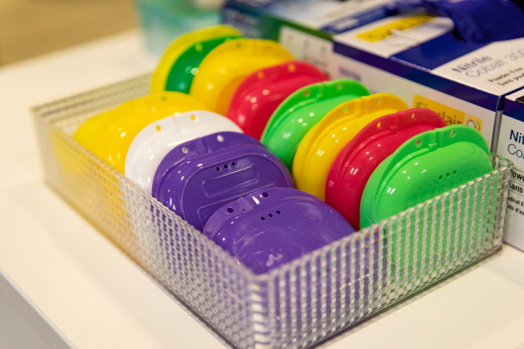 A clear acrylic container holds colorful dental care devices in various shades of purple, yellow, red, green, and white, neatly organized for easy access.