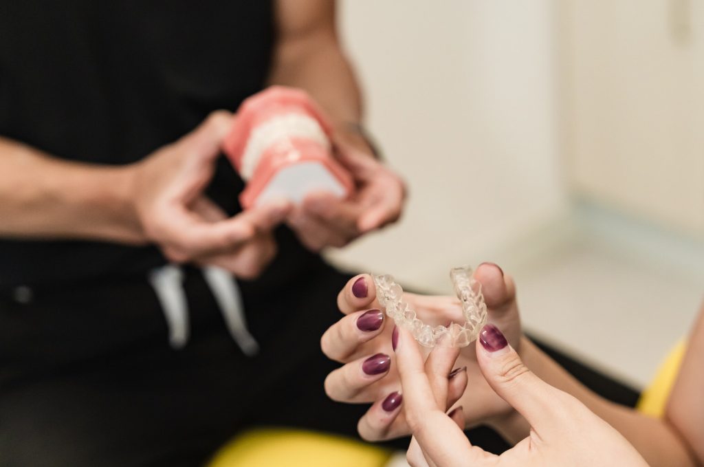 A dental professional demonstrates an orthodontic appliance while a patient holds a similar device, showcasing a dental consultation. The scene conveys a focus on oral care, emphasizing personalized treatment.