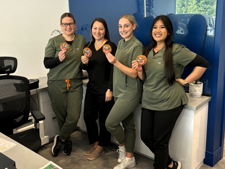 Four dental team members in green scrubs smile while holding colorful tokens in an office setting. The atmosphere is friendly and inviting, showcasing team spirit. The 123Dentist Smiley is also present, adding a cheerful touch to the scene.