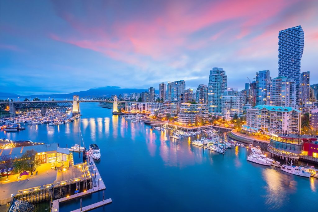 A vibrant cityscape of Vancouver at twilight with illuminated buildings along the waterfront and a scenic pink and blue sky, suggesting a great spot to find a dentist near you.