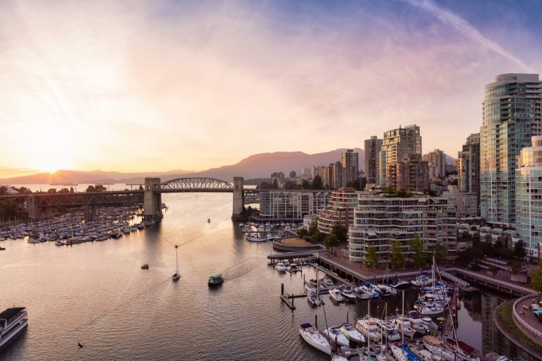 Sunset view of a city harbor with boats and skyscrapers, featuring a bridge in the background and a large smiling face icon in the sky.
