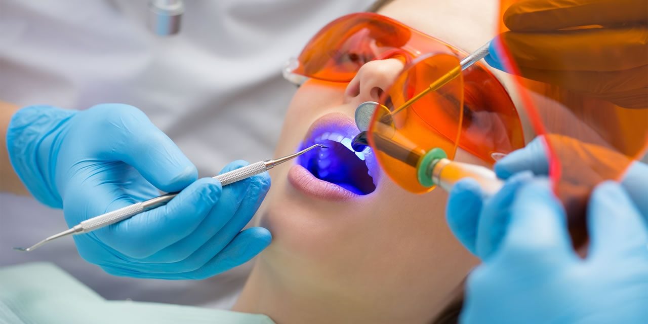 Dental professional applying blue UV light treatment to patient's tooth during restorative procedure at our clinic